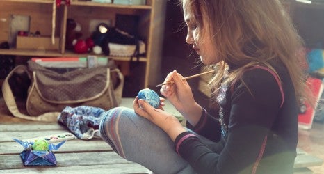 Little girl paints egg for Easter day indoors