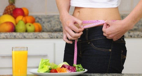 woman eating salad and fruits and measuring her waist